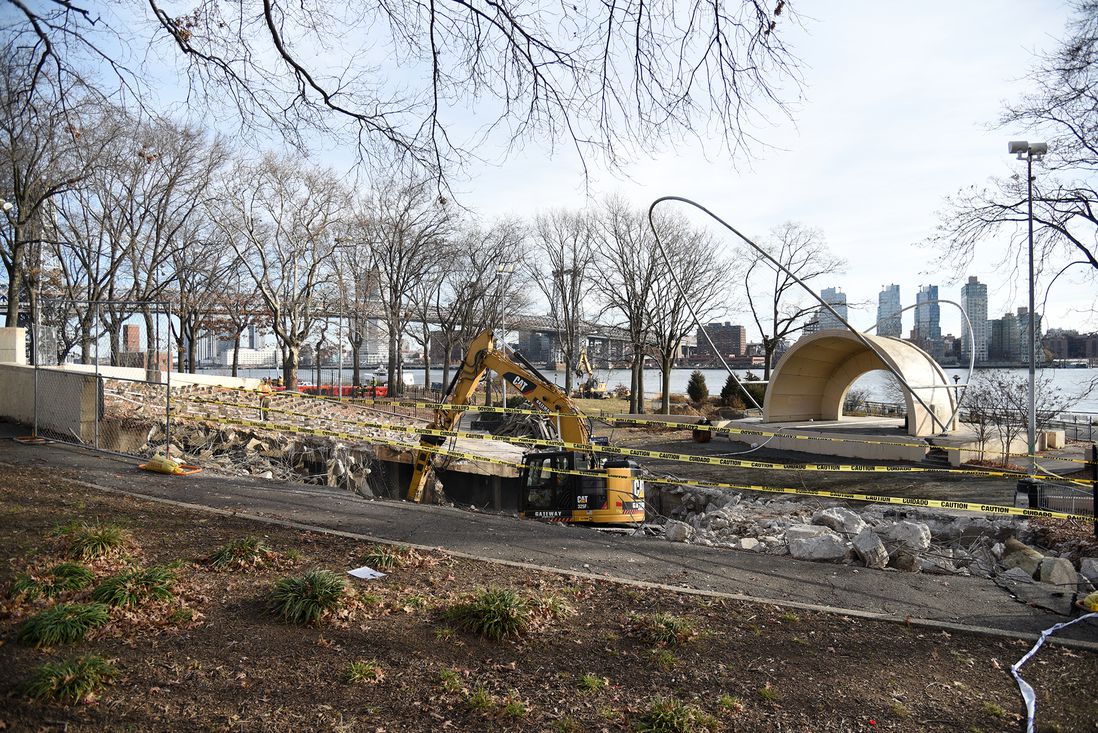 An excavator removes the concrete seating area at the historic amphitheater, while loggers chainsaw the last trees in the southern part of East River Park, around the amphitheater.